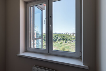 The window in the apartment overlooks the green forest and the blue sky