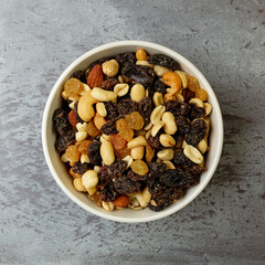 Top view of a bowl filled with high energy trail mix on a gray mottled background in natural light. - 615063763