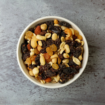 Top view of a bowl filled with high energy trail mix on a gray mottled background in natural light.