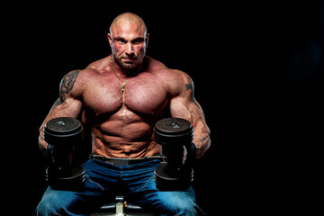 Strong Shirtless Bodybuilder wearing jeans and lifting Dumbbells