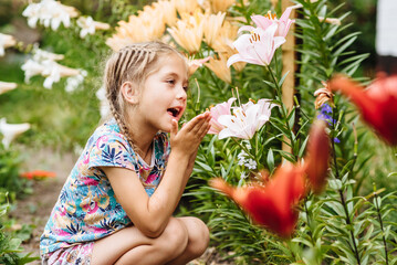 A little girl in the garden sniffs white lily flowers. Spring blooming concept. The child is having fun in the summer blooming garden of the garden. Childhood, harmony with nature, aromatherapy.