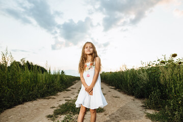 A beautiful girl poses against the background of blooming sunflowers. A cute child in a white dress is running and jumping in a meadow at sunset. Happy childhood, harmony with nature.