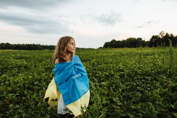 A girl works in a sunflower field with a Ukrainian yellow-blue flag. The concept of support and assistance to Ukraine. Independence Day. Children are our future