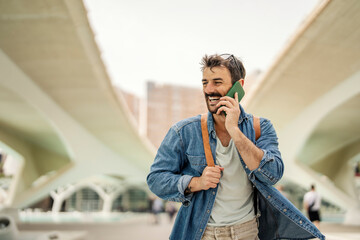 A happy retro man is walking on the street with urban architecture and talking on the phone.