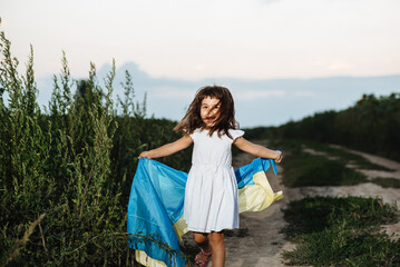 A happy child runs in a meadow with a yellow-blue flag of Ukraine. Soft focus