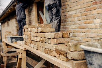 Selective focus on pile of bricks on a scaffolding with builders making a house.