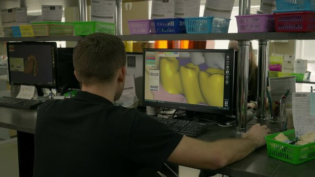 Dental technician using modern 3D computer program. Dental technician looks at the teeth inside the program. Dental technician operating the program to model the artificial replacement teeth.
