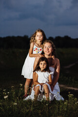 A mother and two daughters pose in white dresses at sunset. Family on vacation outside the city. Portrait of a woman with two children in nature. The concept of Mother's Day is family.