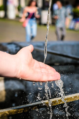 Girl's hands and flowing water at the water fountain in town