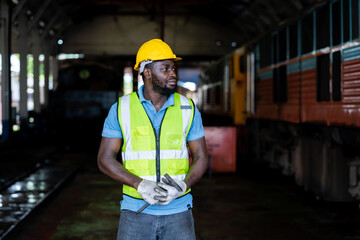 Portrait of African male railway engineer standing confidently with green safety suit and helmet. Workers working at heavy machinery at industrial plant.