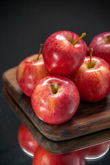 Vertical view of fresh red apples on wooden cutting board on dark color background
