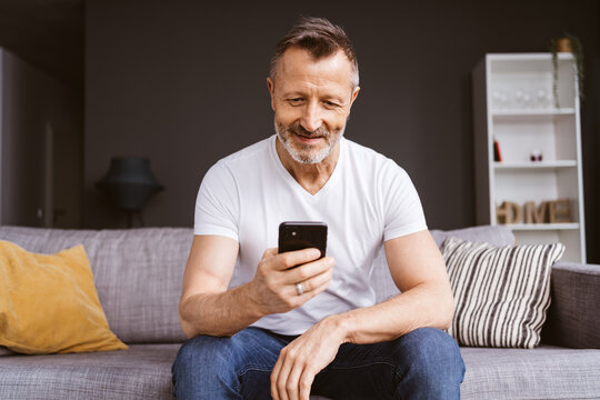 Older Man in White T-Shirt Sitting looking at his Smartphone on the Sofa