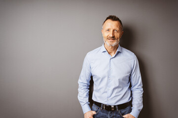 Relaxed Older Businessman in Blue Shirt Standing in Front of a Brown Wall, Looking into the Camera with Copy Space