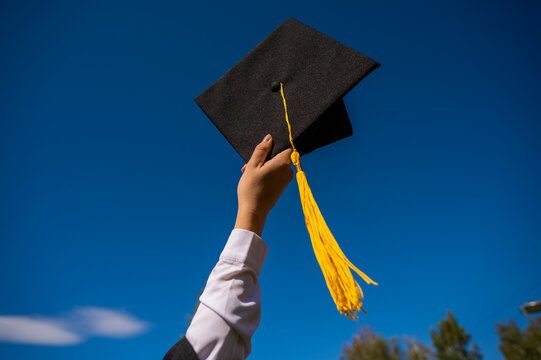 Close-up of a woman's hand with a graduation cap against the blue sky. 