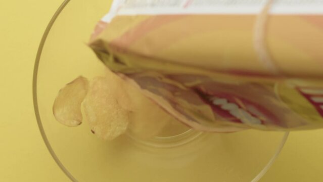 Slow-motion, potato chips falling from a packet into a plate 