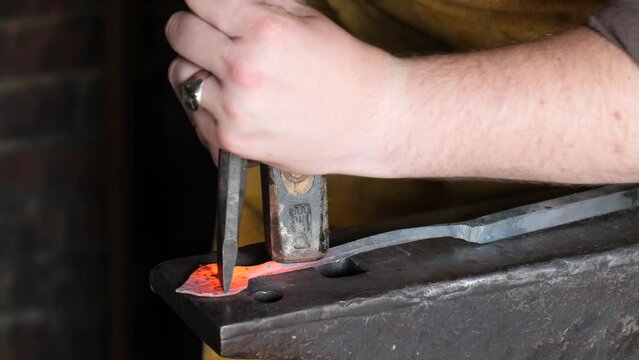 Blacksmith stokes a coal fire and pounds a red hot peice of metal with a hammer