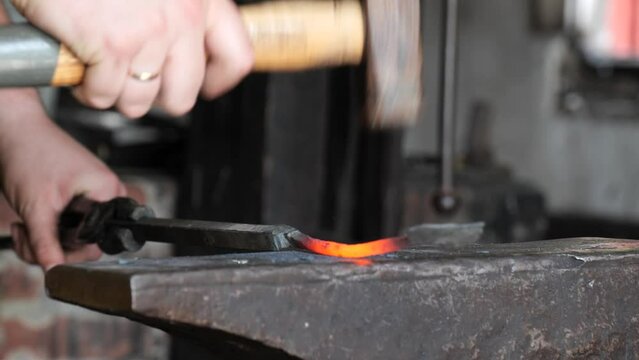 Blacksmith stokes a coal fire and pounds a red hot peice of metal with a hammer