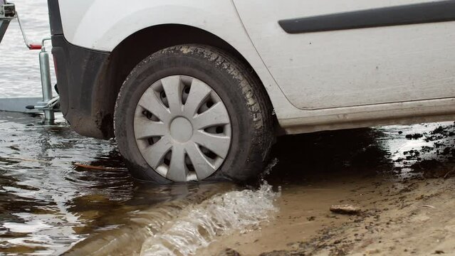 a close-up of a car standing in the water and ready to pull a trailer with a boat from a river or lake