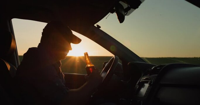 Silhouette of a man who drinks beer while driving a car