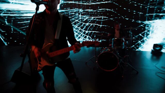 Jib shot of a rock band playing the gig during concert on stage of a large venue, surrounded by bright flashing stage lights