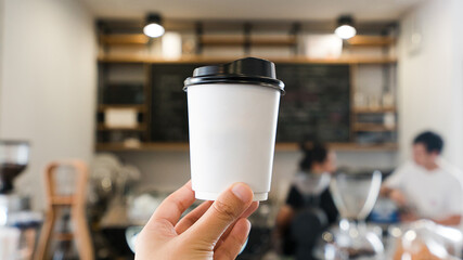 Mockup of hand holding a Coffee paper cup with cafe blur background. Coffee take away. Eco concept.