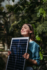 Young woman in jungle holding paper model of house with solar panels, concept of renewable energy...