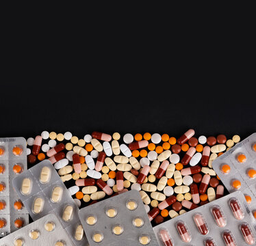Heap of medicine pills, top view image heap of medicine pills. Bottom half full top half empty copy space area, isolated on black background. Full blister packs with colorful drugs. Pharmacy theme.
