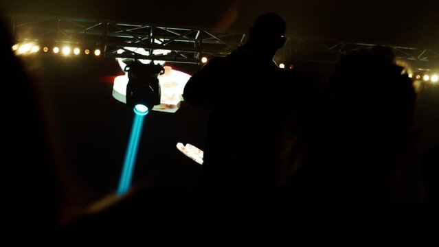 African-American Black rap artist performing his gig in front of a concert crowd on a stage of a large venue, surrounded by bright flashig lights
