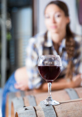 girl looking at glass of red wine standing on wooden barrel in winery