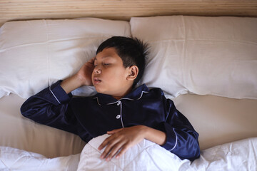Tranquil little boy wear pajamas sleeping on soft pillow under warm blanket, relaxing on white...