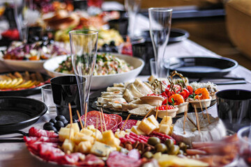 Festive wedding table with appetizer, salad, cheese, sausage, beef and pork, fruit, with a goblet and glass, plate close-up and blurred background.