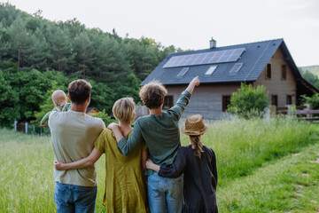 Rear view of family near their house with solar panels. Alternative energy, saving resources and...