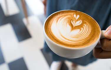 Woman holding a cup of hot coffee latte art in cafe
