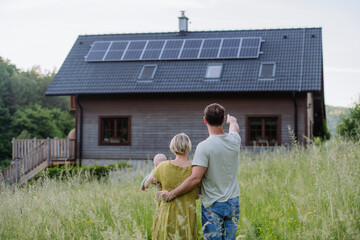 Rear view of family near their house with solar panels. Alternative energy, saving resources and...