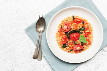 Tomato fried rice has basil in bowl on white slate table