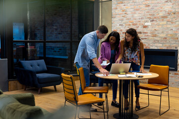 Diverse male and female colleagues in discussion using laptop at casual office meeting