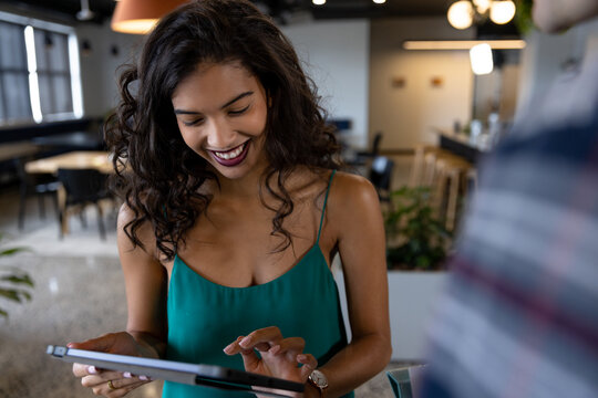 Smiling biracial casual businesswoman using tablet with colleague in office