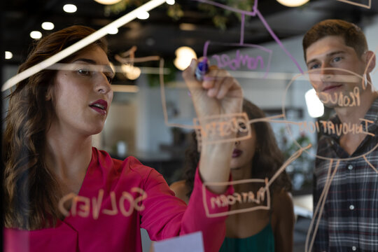 Diverse creative colleagues in discussion brainstorming making notes on glass wall in office
