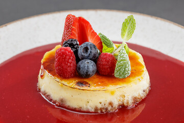 Homemade cheesecake with strawberries, strawberry sauce and blueberries and mint leaves in a white bowl. Shallow depth of field