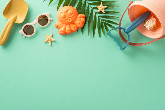 Delightful summer escape with children by the seaside: Top view flat-lay photograph of sand toys for kids, sunglasses, palm leaf and starfish on isolated turquoise background with copyspace