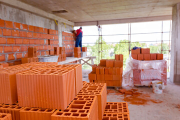 Pile of red blocks on wooden platform, worker build wall with bricks and mortar