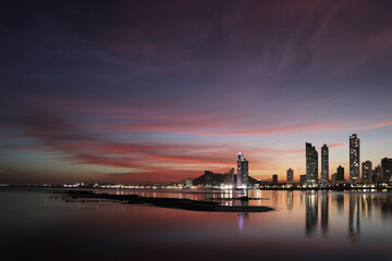 Fototapeta premium sunset over Panama city with reflection of the skyline on the bay's ocean water with dramatic red clouds 