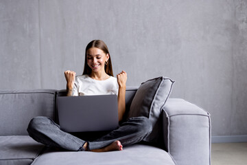 Excited woman using phone and laptop sitting on a couch in the living room at home