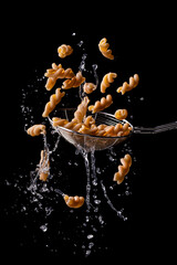 Wholemeal fusilli, Italian pasta floating and dripping on a black background.