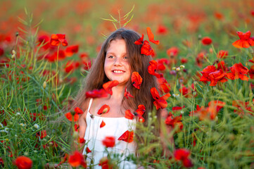 cute girl wearing white dress in summer blooming poppy field walking under evening sun
