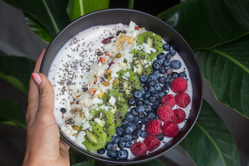 A plate of fresh fruits with yogurt in a girl's hand. Breakfast, snack. Healthy eating and lifestyle concept. Healthy breakfast. Oatmeal with fruits and nuts in a black plate