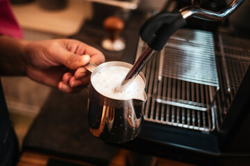 Close-up of Barista hand using high-pressure steam-operated milk frother to prepare a cappuccino...