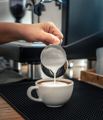barista pouring milk into coffee making cappuccino. Professional barista preparing coffee on the...