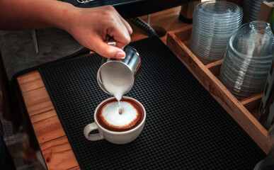 Barista hand pouring milk into coffee making a cappuccino. Professional barista preparing coffee on the counter.