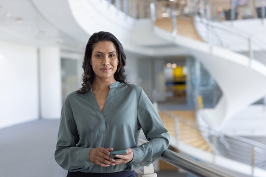 Portrait of a businesswoman holding a smartphone in modern corporate office atrium